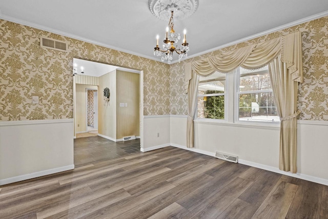 empty room with wood finished floors, a wainscoted wall, visible vents, and wallpapered walls