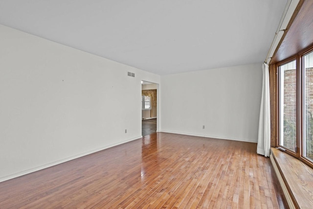 unfurnished room featuring a wealth of natural light, light wood finished floors, visible vents, and baseboards