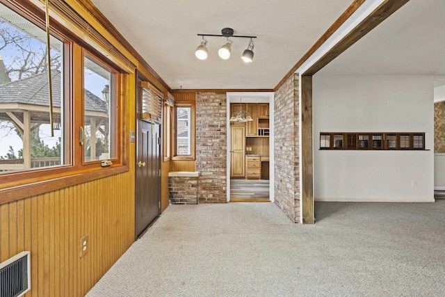 interior space featuring visible vents, brick wall, ornamental molding, carpet flooring, and wood walls