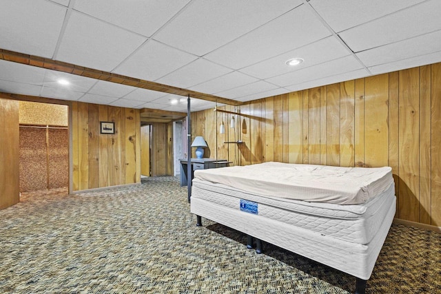 bedroom featuring carpet floors, a drop ceiling, and wooden walls