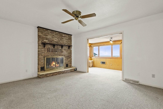 unfurnished living room with carpet floors, a fireplace, visible vents, and a ceiling fan