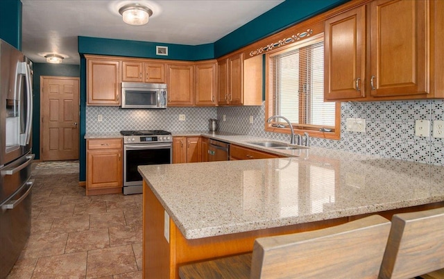 kitchen with light stone counters, a peninsula, a sink, appliances with stainless steel finishes, and tasteful backsplash