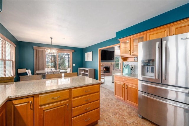 kitchen with a stone fireplace, a notable chandelier, stainless steel fridge with ice dispenser, decorative backsplash, and glass insert cabinets