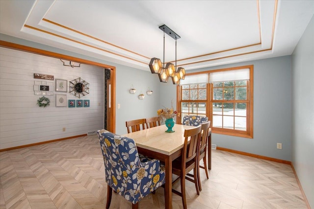 dining area featuring a notable chandelier, wooden walls, a raised ceiling, and baseboards