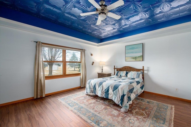 bedroom featuring a raised ceiling, baseboards, and wood finished floors