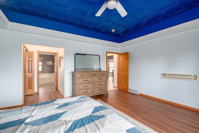 bedroom with baseboards, visible vents, ensuite bath, wood finished floors, and a tray ceiling