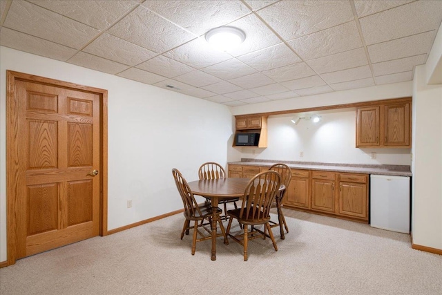 dining room with baseboards, a drop ceiling, and light colored carpet