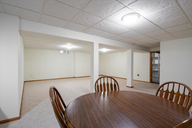 carpeted dining room with a paneled ceiling and baseboards