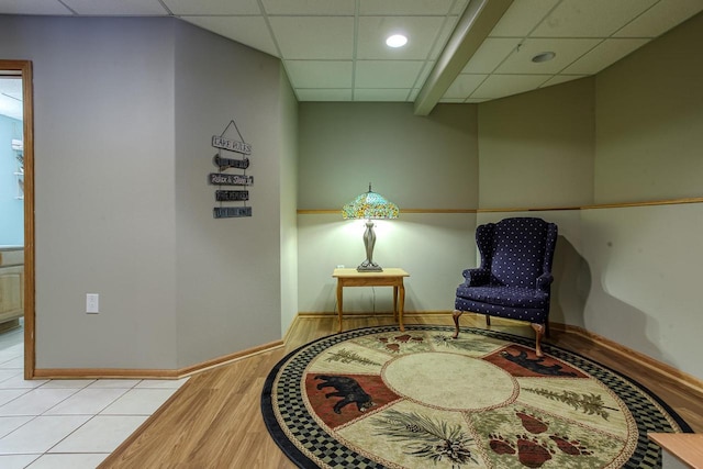 living area featuring light wood-style floors, a paneled ceiling, and baseboards