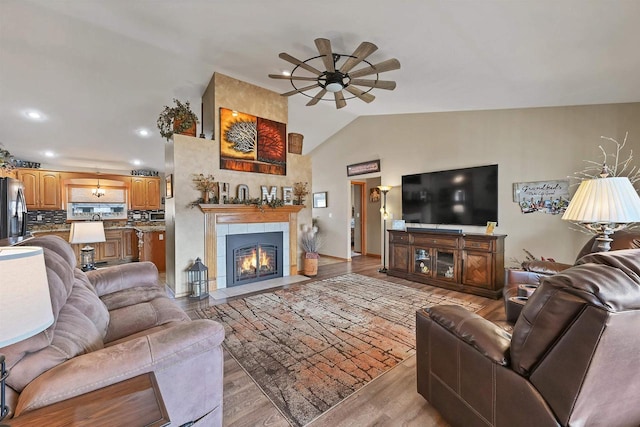 living area featuring a tile fireplace, light wood-style flooring, recessed lighting, a ceiling fan, and vaulted ceiling