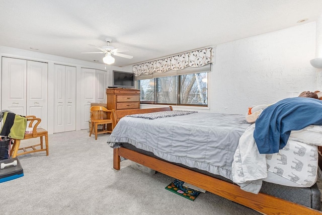 bedroom with carpet, multiple closets, a textured wall, ceiling fan, and a textured ceiling