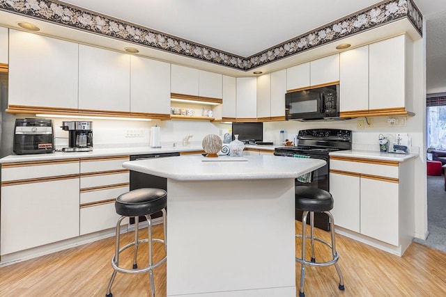 kitchen featuring black appliances, light wood finished floors, a kitchen bar, and light countertops