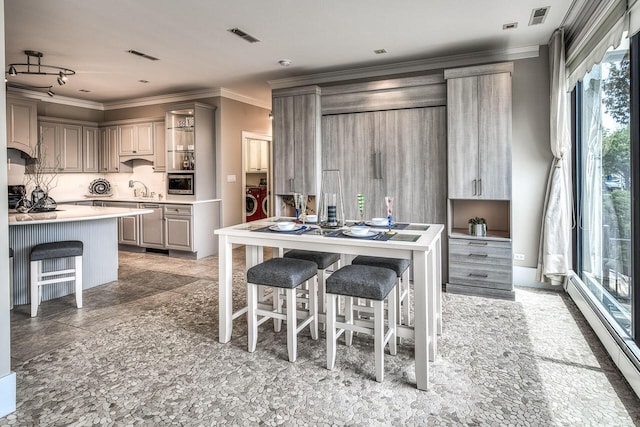 kitchen featuring a breakfast bar, crown molding, light countertops, stainless steel microwave, and a baseboard heating unit