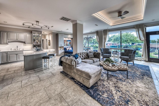 living area featuring a raised ceiling, visible vents, ornamental molding, a ceiling fan, and ornate columns