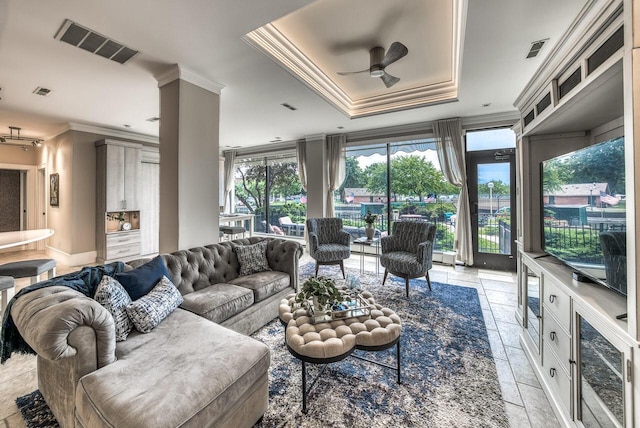 living area featuring stone tile floors, visible vents, a ceiling fan, ornamental molding, and a tray ceiling