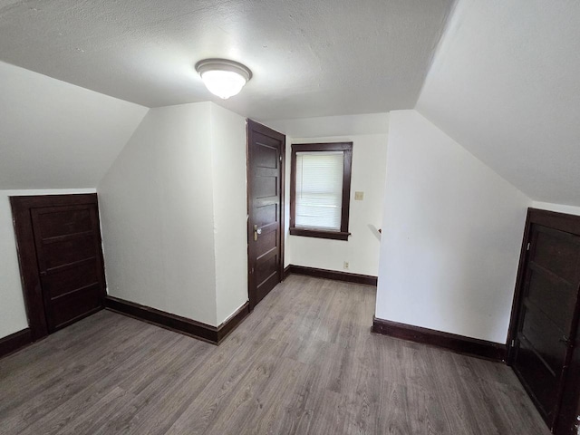 additional living space featuring a textured ceiling, baseboards, and wood finished floors