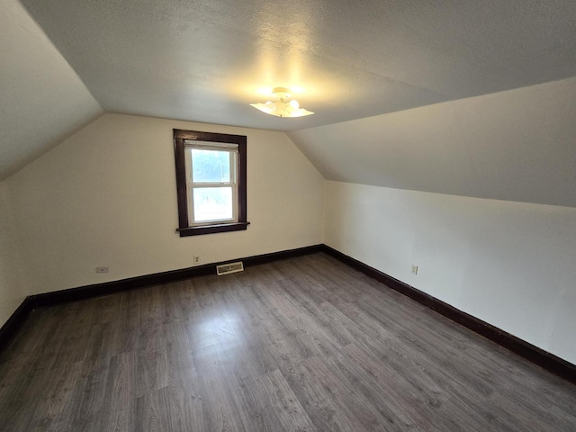 bonus room with a textured ceiling, visible vents, baseboards, vaulted ceiling, and dark wood finished floors