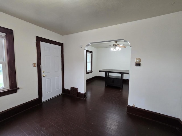 unfurnished room featuring a ceiling fan, baseboards, arched walkways, and dark wood-type flooring