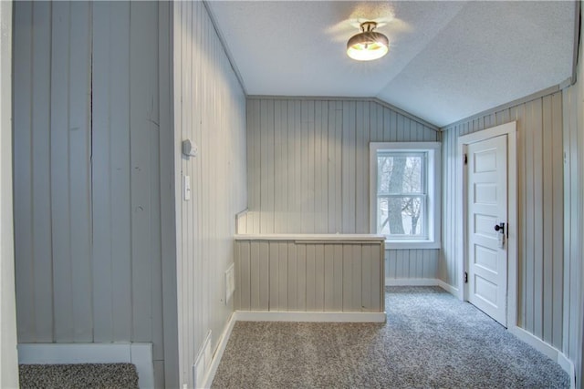 bonus room with a textured ceiling, wooden walls, carpet floors, baseboards, and vaulted ceiling