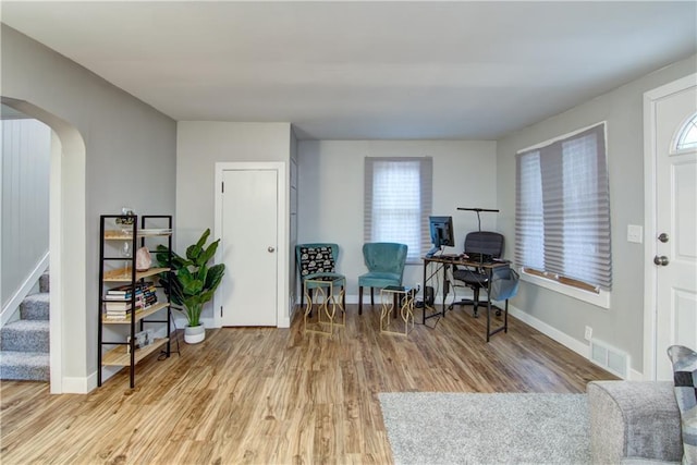 living area with light wood-style floors, arched walkways, a wealth of natural light, and stairs