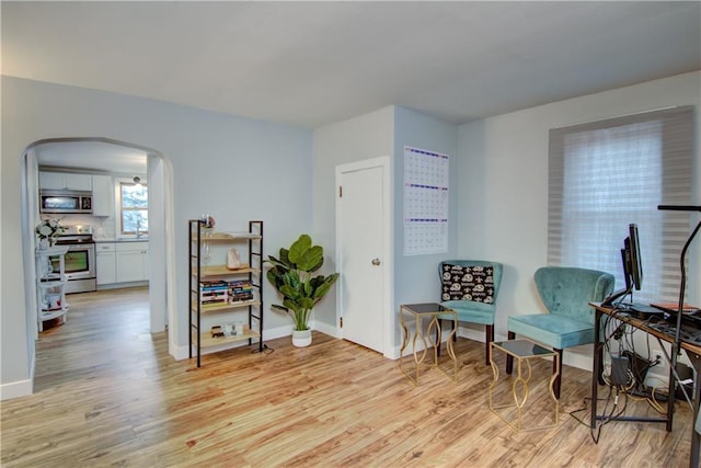 sitting room featuring light wood-style flooring, arched walkways, and baseboards