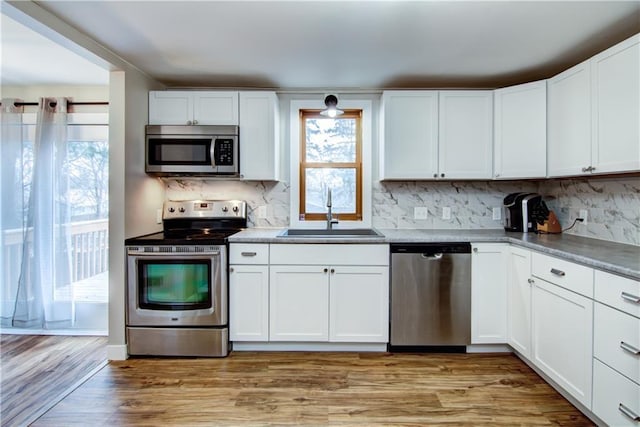 kitchen featuring stainless steel appliances, decorative backsplash, light wood-style floors, white cabinetry, and a sink