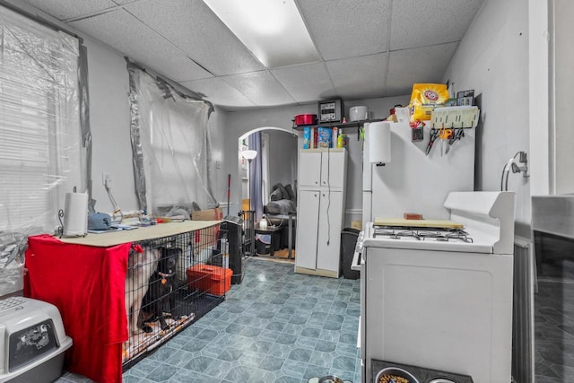 kitchen with white gas range, arched walkways, a drop ceiling, and tile patterned floors