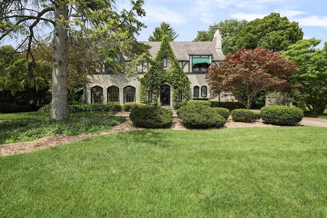 tudor home with stone siding, a chimney, and a front lawn