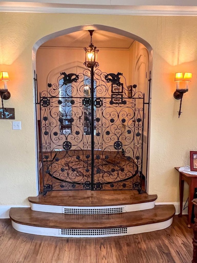 room details featuring arched walkways, a textured wall, wood finished floors, and baseboards