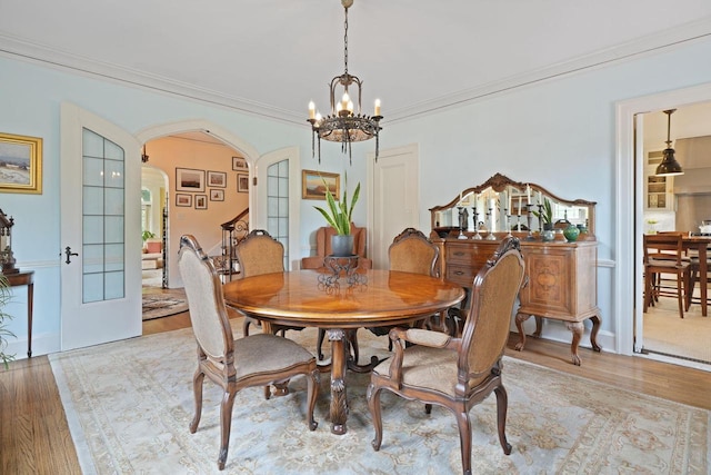 dining room with light wood-type flooring, arched walkways, a chandelier, and ornamental molding