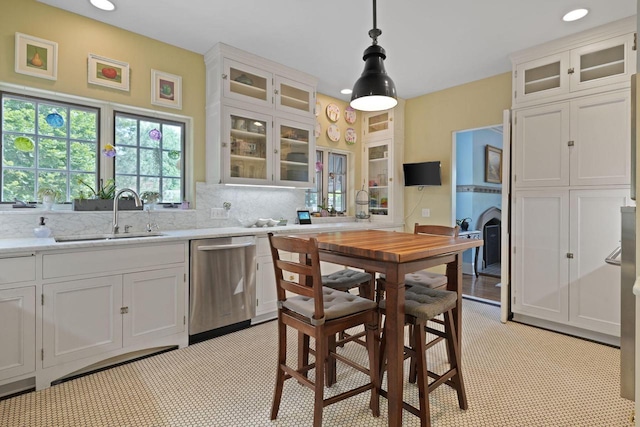 kitchen featuring stainless steel dishwasher, backsplash, a sink, and white cabinetry