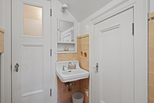 bathroom with vaulted ceiling, a sink, tile walls, and decorative backsplash