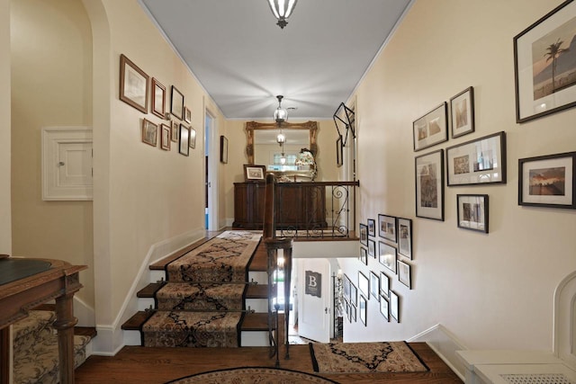 hallway featuring arched walkways, stairway, and baseboards