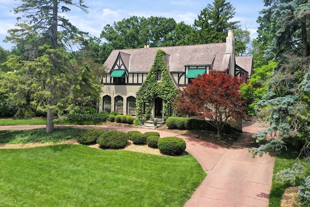 tudor house with stone siding, a front lawn, a chimney, and stucco siding