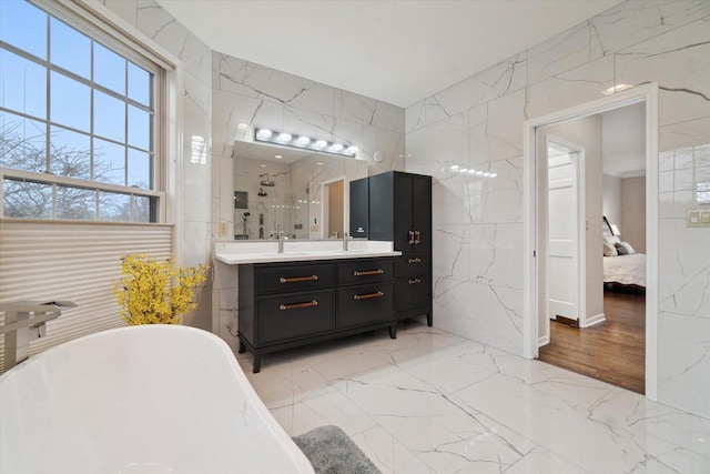 bathroom featuring marble finish floor, walk in shower, vanity, and stone wall