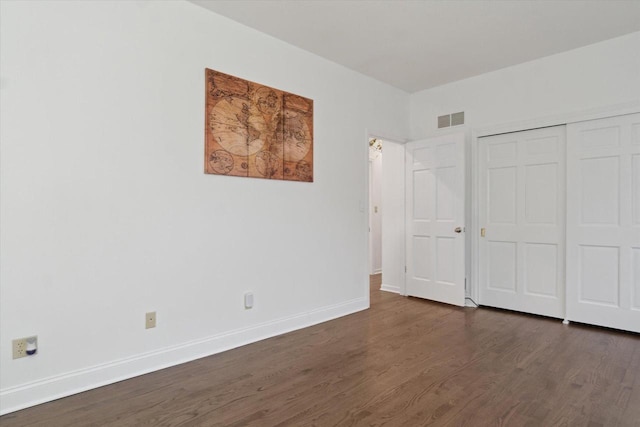 unfurnished bedroom with dark wood-style flooring, a closet, visible vents, and baseboards