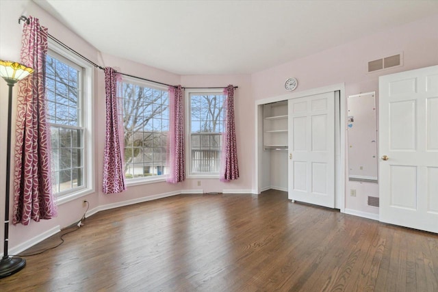 unfurnished bedroom with dark wood-style flooring, visible vents, baseboards, and multiple windows