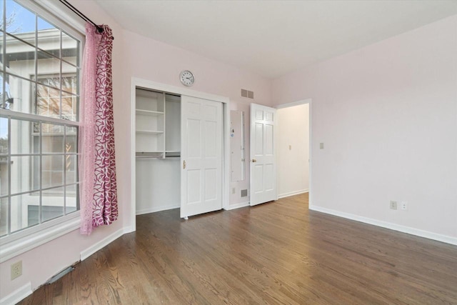 unfurnished bedroom featuring a closet, visible vents, baseboards, and wood finished floors