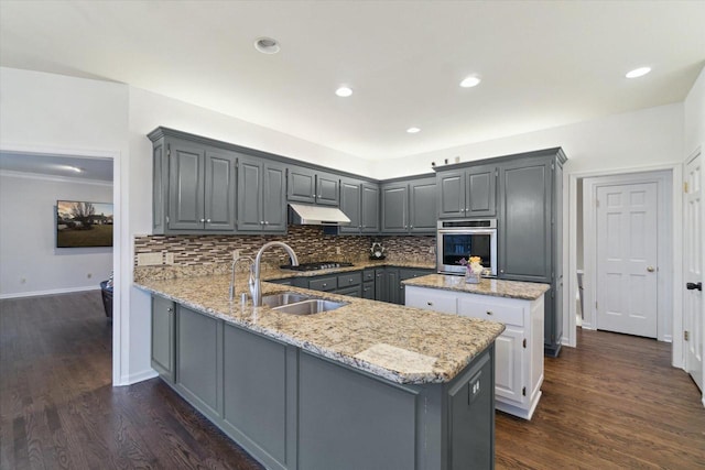 kitchen featuring tasteful backsplash, gray cabinetry, under cabinet range hood, stainless steel oven, and a sink