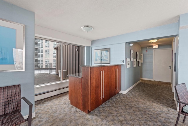 interior space with a baseboard heating unit, a textured ceiling, dark carpet, brown cabinetry, and baseboards