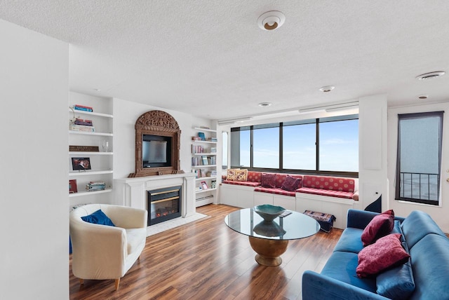 living area featuring a fireplace with flush hearth, wood finished floors, built in shelves, and a textured ceiling