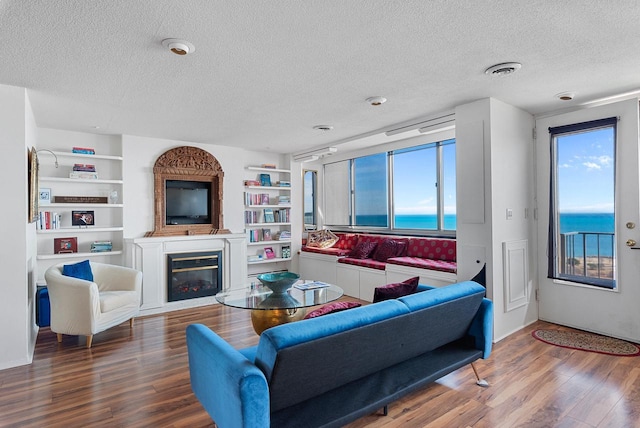 living room with visible vents, built in features, wood finished floors, a glass covered fireplace, and a textured ceiling