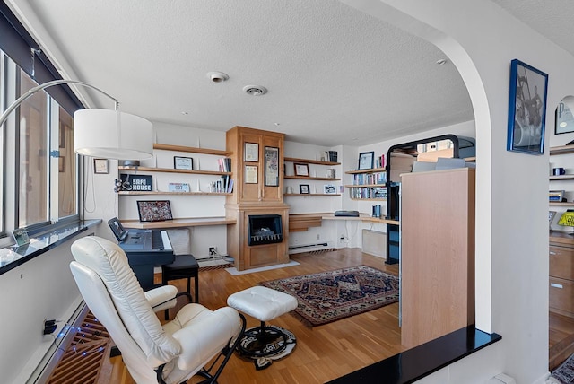 living room featuring a baseboard heating unit, baseboard heating, wood finished floors, arched walkways, and a textured ceiling