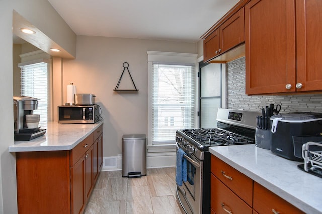 kitchen with appliances with stainless steel finishes, brown cabinetry, light stone counters, and decorative backsplash