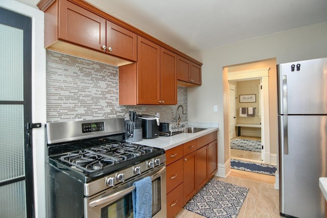 kitchen with light countertops, backsplash, appliances with stainless steel finishes, brown cabinetry, and a sink