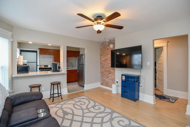 living room featuring light wood finished floors, a ceiling fan, and baseboards