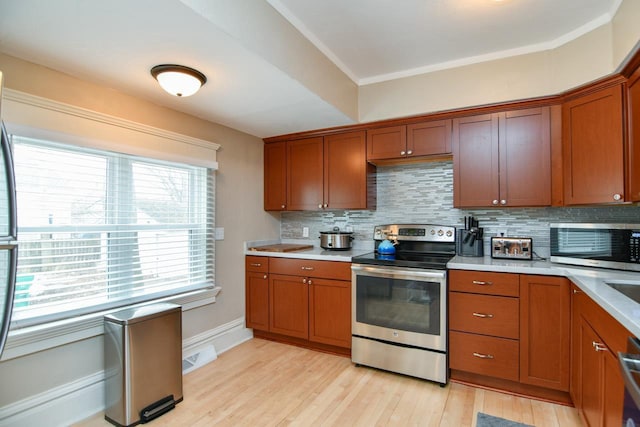 kitchen with light wood-style floors, appliances with stainless steel finishes, light countertops, and decorative backsplash