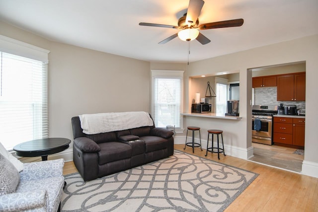 living area featuring a ceiling fan, baseboards, and light wood finished floors