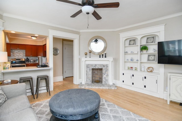 living area featuring light wood finished floors, ceiling fan, ornamental molding, and a fireplace with raised hearth