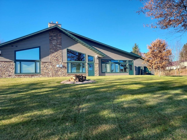 back of property with stone siding, a lawn, and a chimney